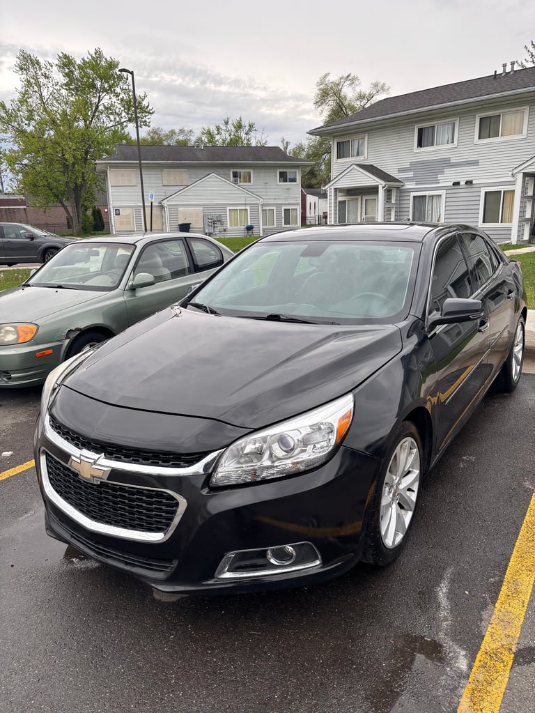 Black Chevrolet Malibu parked in a residential driveway with houses and trees in the background