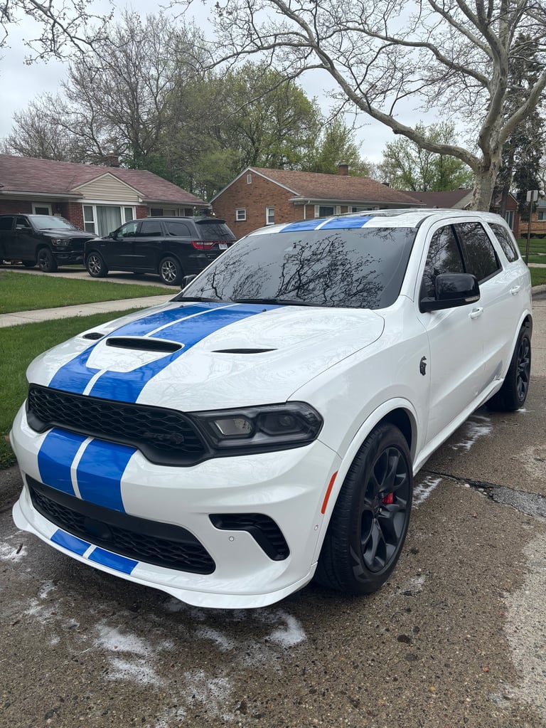 White Dodge Durango with blue racing stripes parked in a residential driveway with brick houses in the background